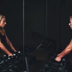 Gym Storage Solutions - woman wearing black top top holding black dumbbells standing in front of mirror