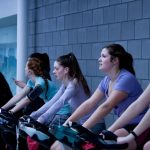Treadmill Elliptical - women taking exercise on black stationary bikes in front of gray concrete wall