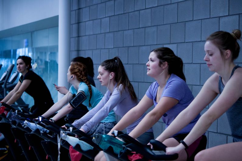 Treadmill Elliptical - women taking exercise on black stationary bikes in front of gray concrete wall